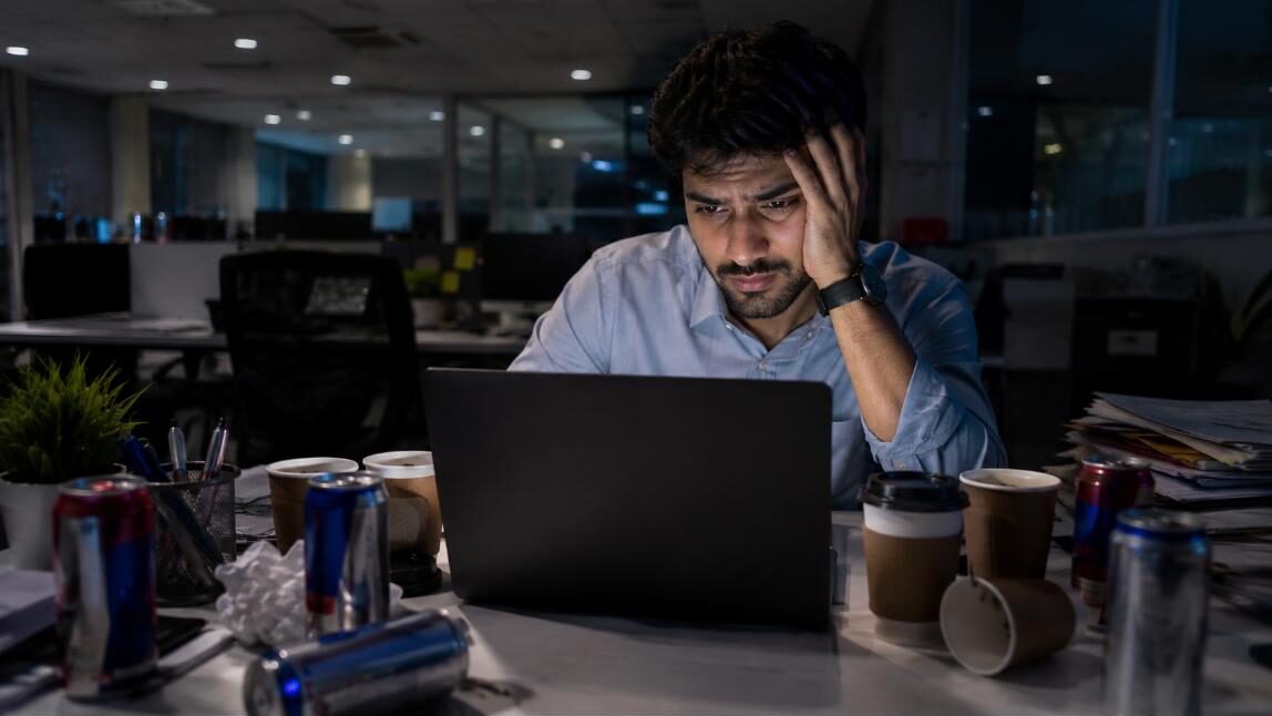 Exhausted Indian corporate professional working late at night surrounded by empty energy drinks and coffee cups